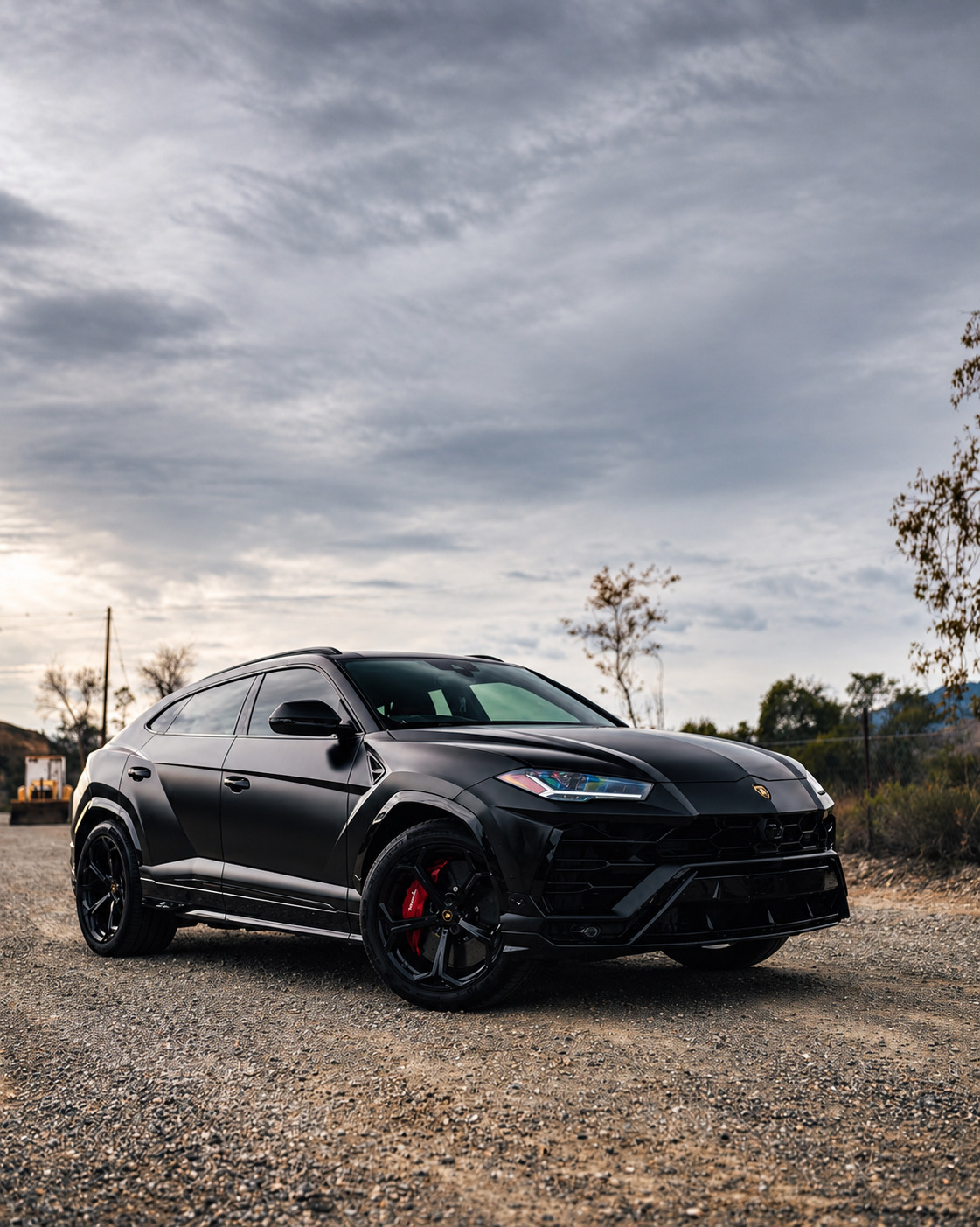 Matte black Lamborghini Urus on gravel beneath an overcast sky